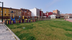 En legeplads med farverigt legetøj, græsplæne og bygninger i baggrunden.