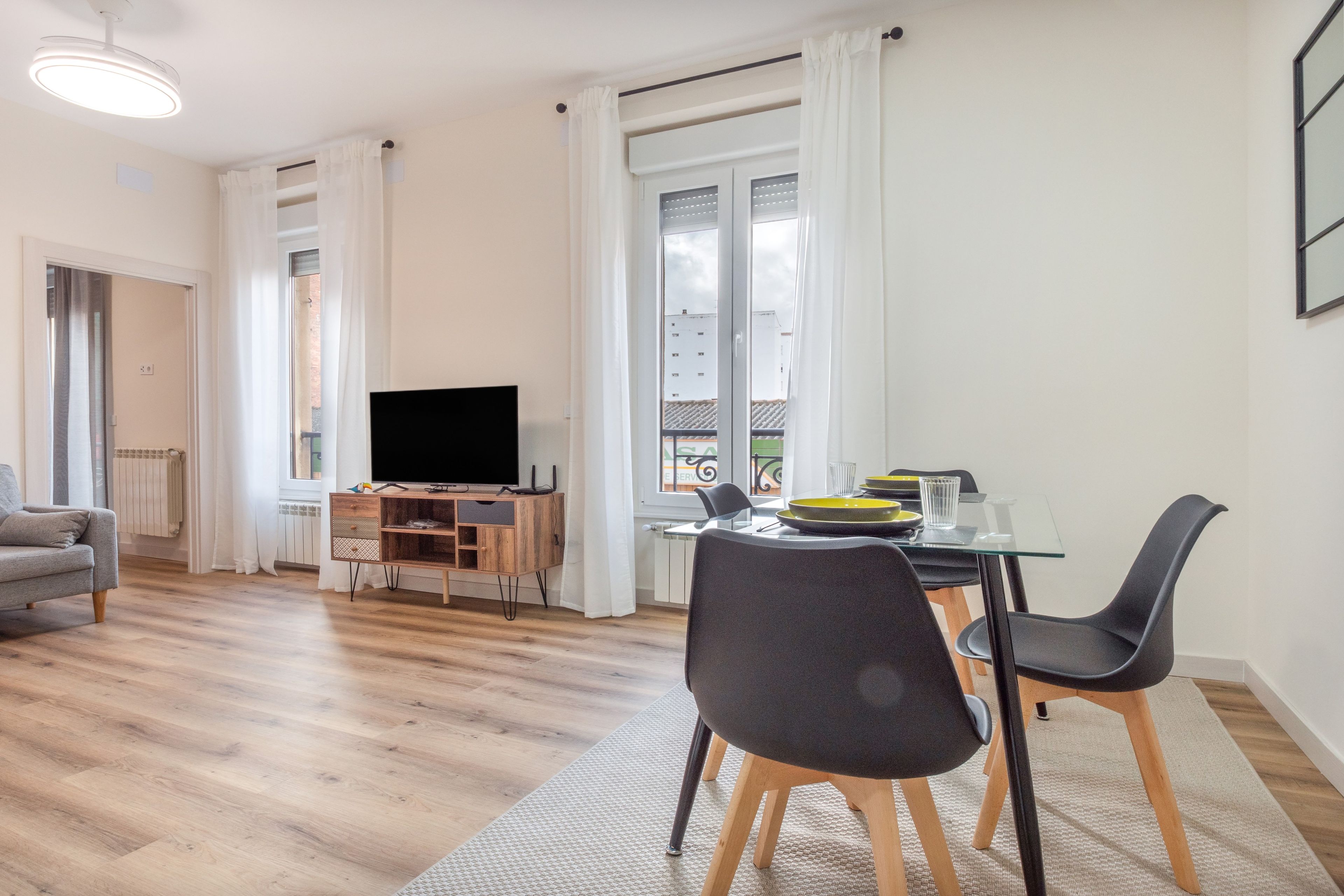 A modern living room with a flat-screen TV, a dining area with a glass table, and a sofa.