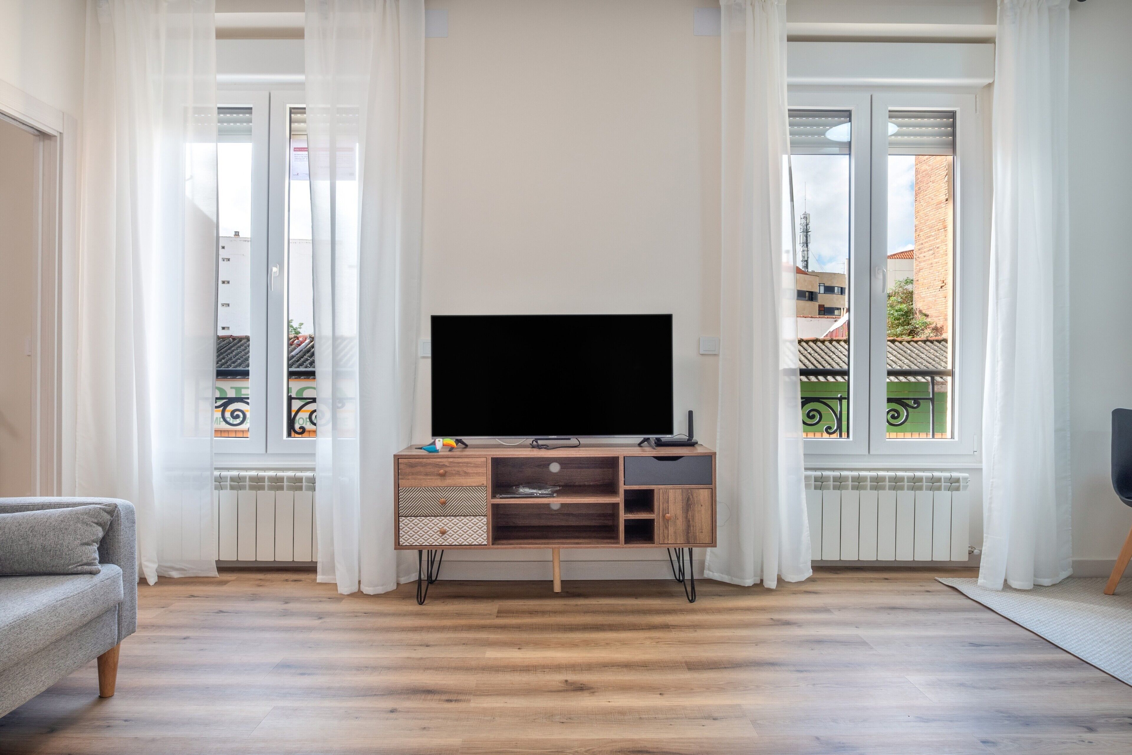 Ein Wohnzimmer mit einer Holz-Unterhaltungsanlage, einem Flachbildfernseher und einem grauen Sofa.
