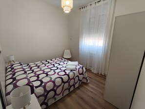 A bedroom with a bed, a bedside table, a lamp, a chair, and a wardrobe.