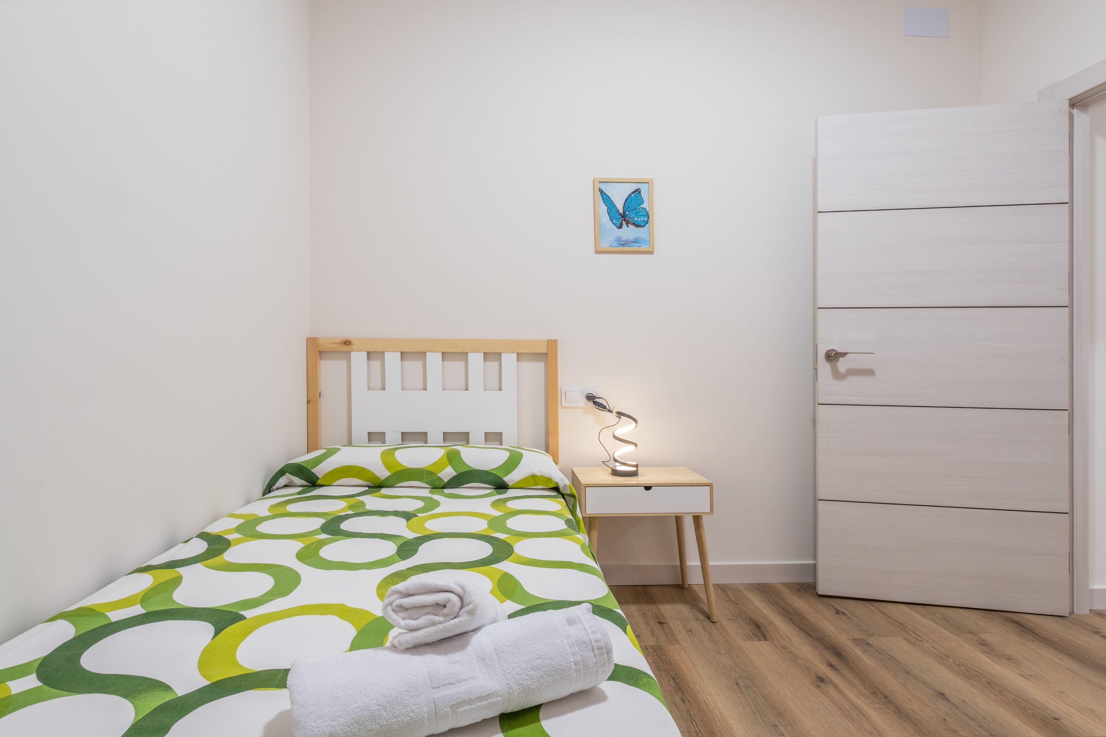 A neatly made bed with a patterned bedspread, a bedside table with a lamp, and a door to the right.