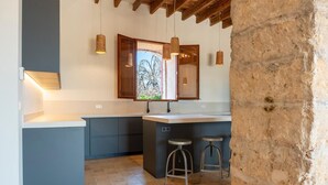 A modern kitchen with a large island, bar stools, pendant lighting, and a view through a window. - S' Hort de ca'n salvà (Santa Maria del Camí)