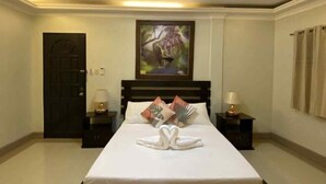 A hotel room with a bed, two nightstands, a door, a painting, and a towel arrangement. - Bohol Casa Nino Alona Resort (Panglao)
