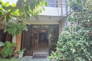 Entrada d'un edifici modern amb portes de vidre, una petita zona de jardí amb plantes en testos i una escala metàl·lica.