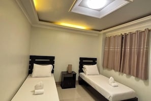 A hotel room with two single beds, a nightstand, a lamp, and a window with curtains.