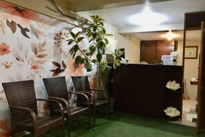 A reception area with a reception desk, three wicker chairs, a large potted plant, and a green carpet. - Bohol Casa Nino Alona Resort (Panglao)