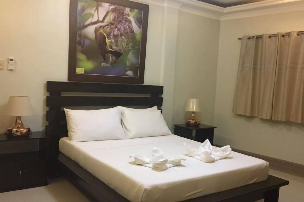 A hotel room with a bed, a nightstand, a lamp, a painting, and a window with curtains.