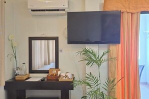 Una habitación con una televisión montada, un espejo, una mesita de consola con objetos decorativos y una planta en maceta.