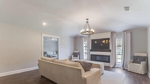 Una sala de estar moderna con un sofá color crema, una chimenea, un televisor y una araña.