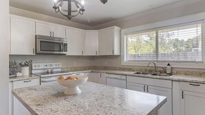 Una cocina moderna con armarios blancos, encimeras de granito, electrodomésticos de acero inoxidable y un amplio ventanal que proporciona luz natural.