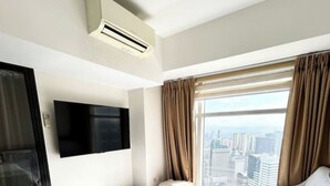 Habitación de hotel con un ventanal grande, un televisor de pantalla plana montado en la pared y un equipo de aire acondicionado.