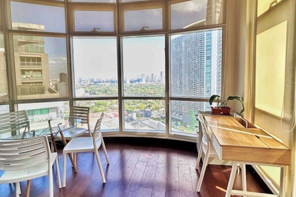 A corner room with large windows, a wooden desk, and white chairs.