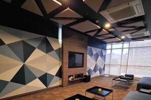 Un salon moderne avec des murs ornés de motifs géométriques, un téléviseur à écran plat et une grande fenêtre laissant entrer la lumière naturelle.