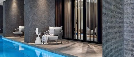 A modern indoor pool area with a seating arrangement and a glass partition wall.