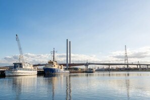 Een jachthaven met aangemeerde boten, een brug op de achtergrond en industriële gebouwen.