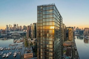 A modern high-rise building with a glass facade, situated near a marina with boats. - Brilliant Collins Wharf Waterfront Condo (Docklands)