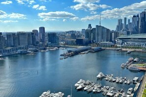 A marina with boats docked, a city skyline in the background, and a large stadium. - Brilliant Collins Wharf Waterfront Condo (Docklands)
