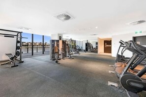 Un gimnasio con equipo cardiovascular, máquinas de pesas y un amplio ventanal con vista a la ciudad.