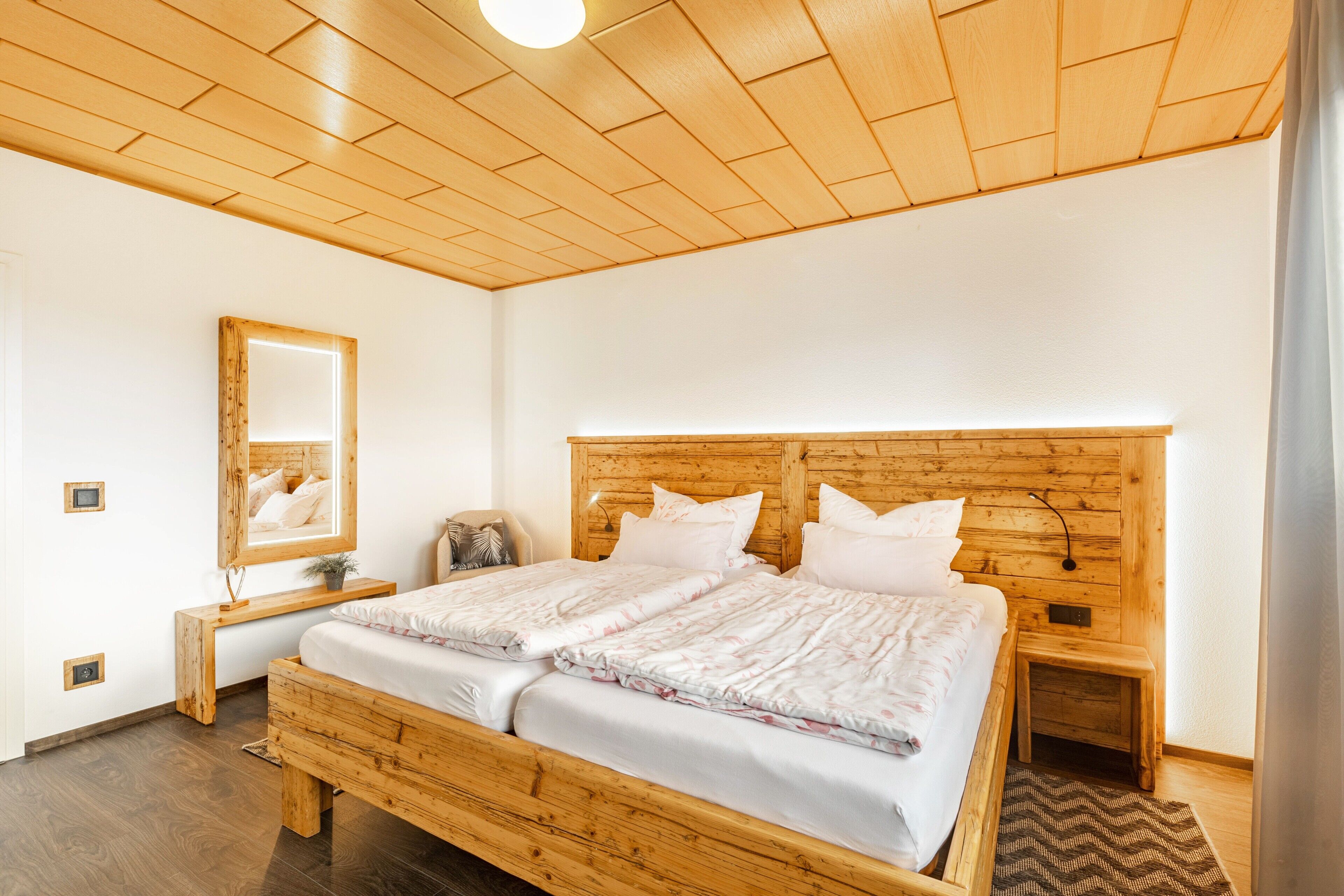 Un lit en bois avec du linge de lit blanc, une table de chevet avec une lampe et un miroir au mur.