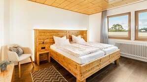 Un letto di legno con biancheria bianca, un comodino, una sedia e vista sull'esterno attraverso ampie finestre.