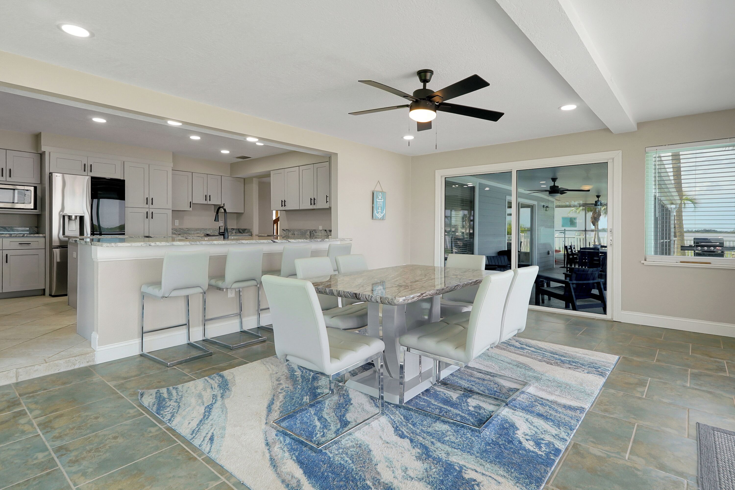 A modern kitchen with white cabinets, a marble island, and a dining area with white chairs.