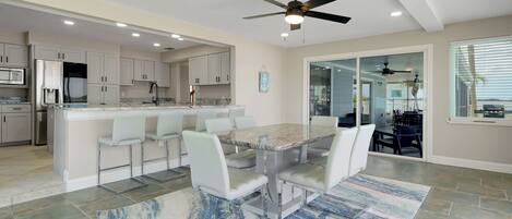 A modern kitchen with white cabinets, a marble island, and a dining area with white chairs.