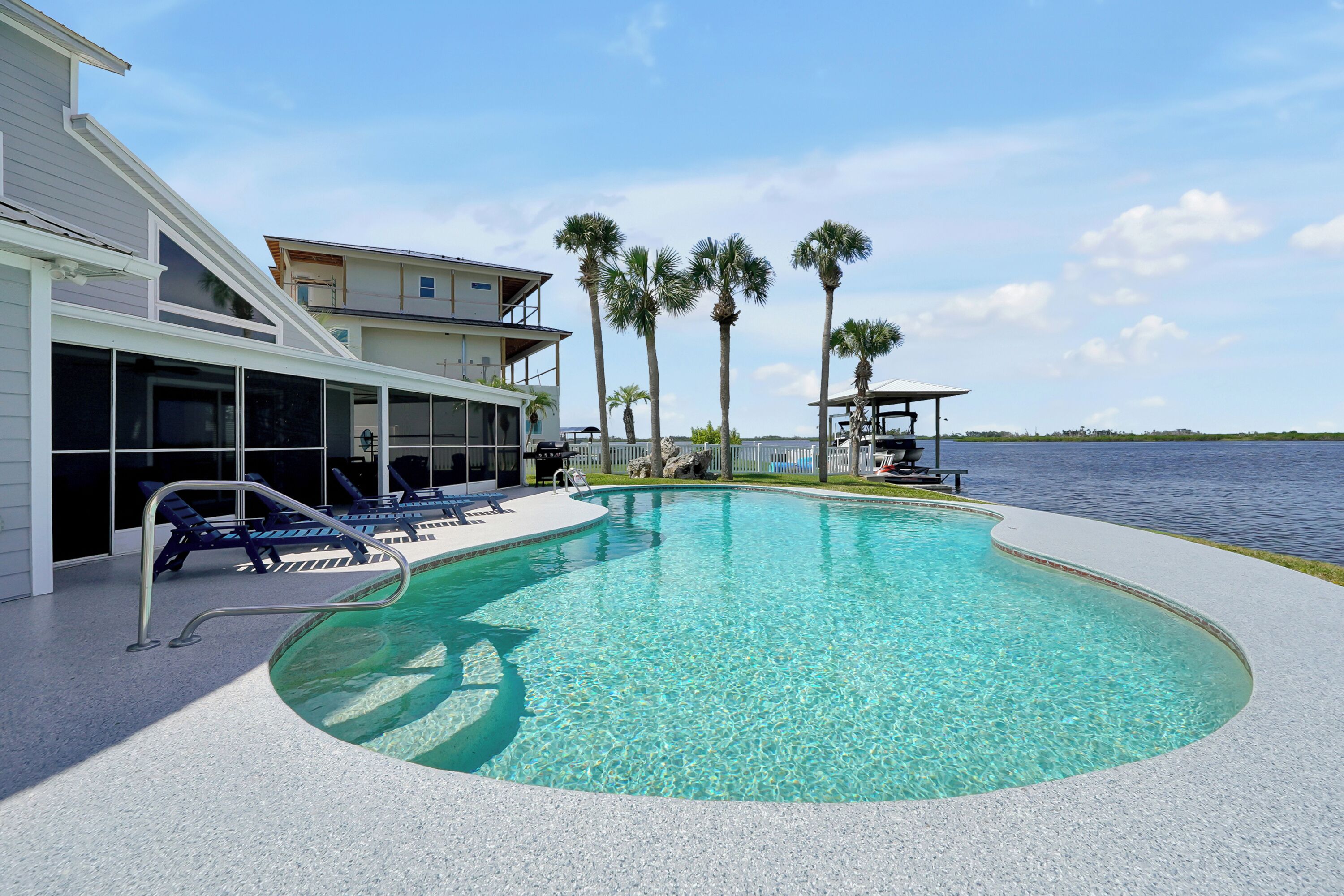 A swimming pool with lounge chairs, a building with balconies, and palm trees.