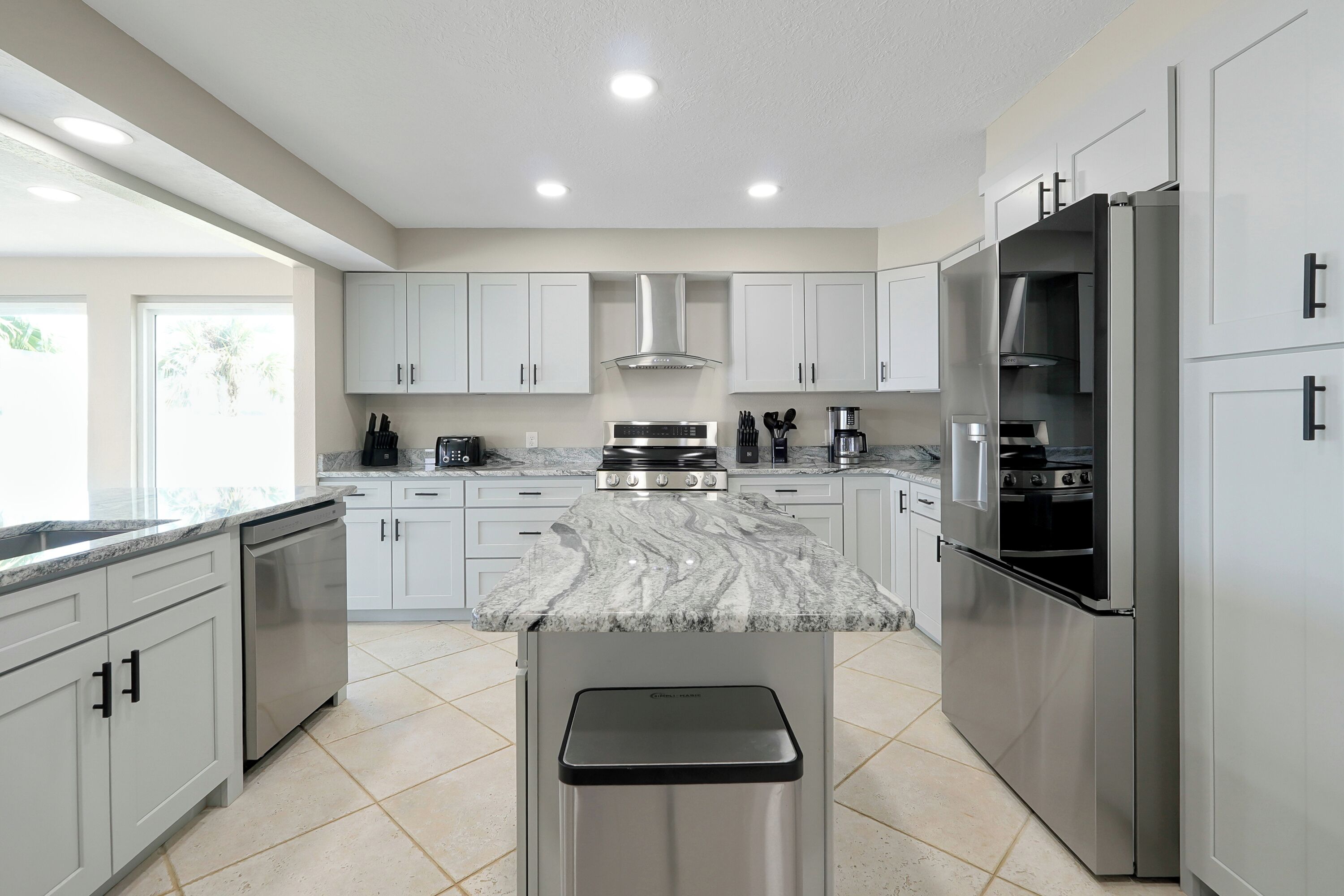 A modern kitchen with white cabinets, stainless steel appliances, and a marble countertop.