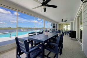 A covered outdoor area with a pool, dining table, chairs, and ceiling fans. - Manatee By The Bay (Crystal River)