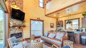 A cozy cabin interior with a stone fireplace, wooden furniture, a kitchen area, and a large window. - Lakeside Bear Lodge (Sevierville)