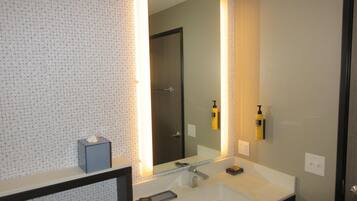 A bathroom with a large mirror, a white sink, and two yellow bottles on the wall.