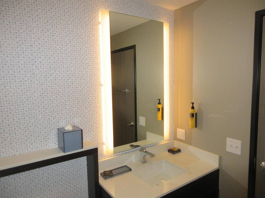 A bathroom with a large mirror, a white sink, and two yellow bottles on the wall.
