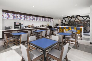 Un café moderno con mesas azules y sillas de madera, una máquina de café y un mostrador con diferentes productos alimenticios.