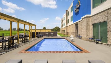 Una piscina con pérgola y zona de estar al aire libre.