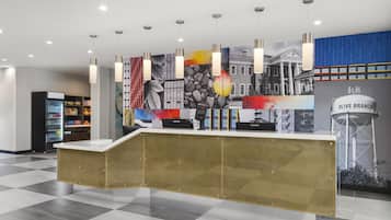Een receptiebalie met een incheckgedeelte, een automaat en een muur met een stadsgezichtsmural.