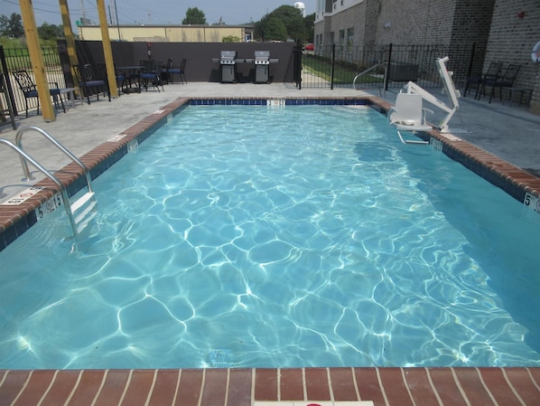 Une piscine rectangulaire à l’eau claire, entourée d’une terrasse en briques et de rampes en métal.