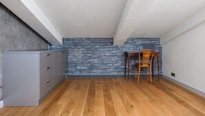Una habitación con suelo de madera, un armario gris, una pared con diseño de ladrillo y una silla de madera.