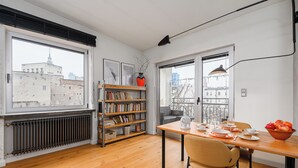 Un comedor con una mesa preparada para dos personas, una estantería y vistas de la ciudad a través de amplios ventanales.