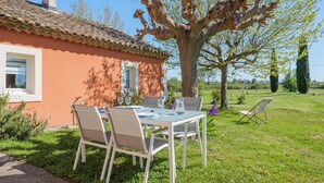 Une maison avec un toit en tuiles, une table avec des chaises et un grand arbre dans la cour.