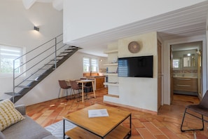 Ein geräumiger Wohnbereich mit Treppe, einem an der Wand befestigten Flachbildfernseher, einem Essbereich und einer Küche.