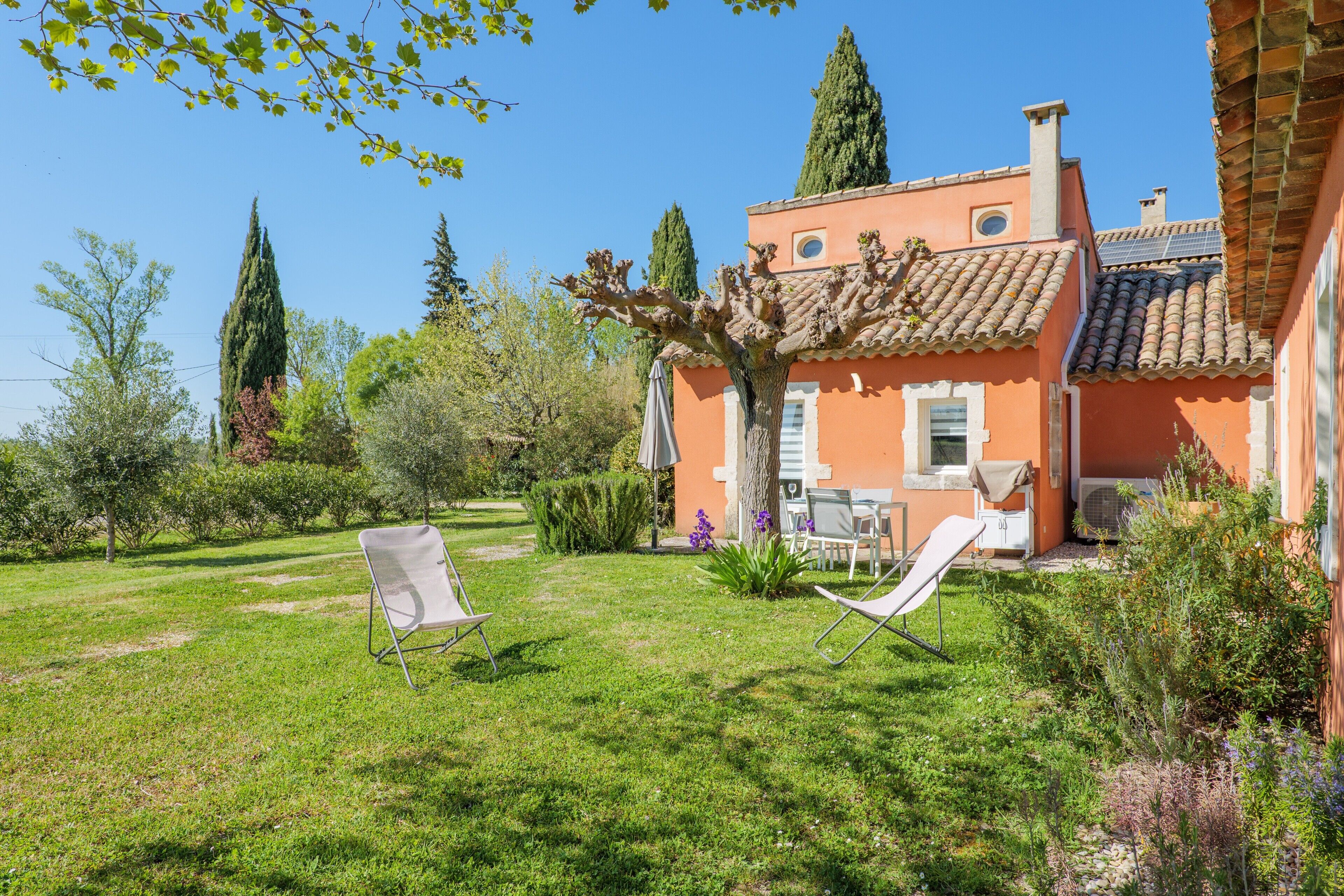 A house with a garden, two lawn chairs, and a table.