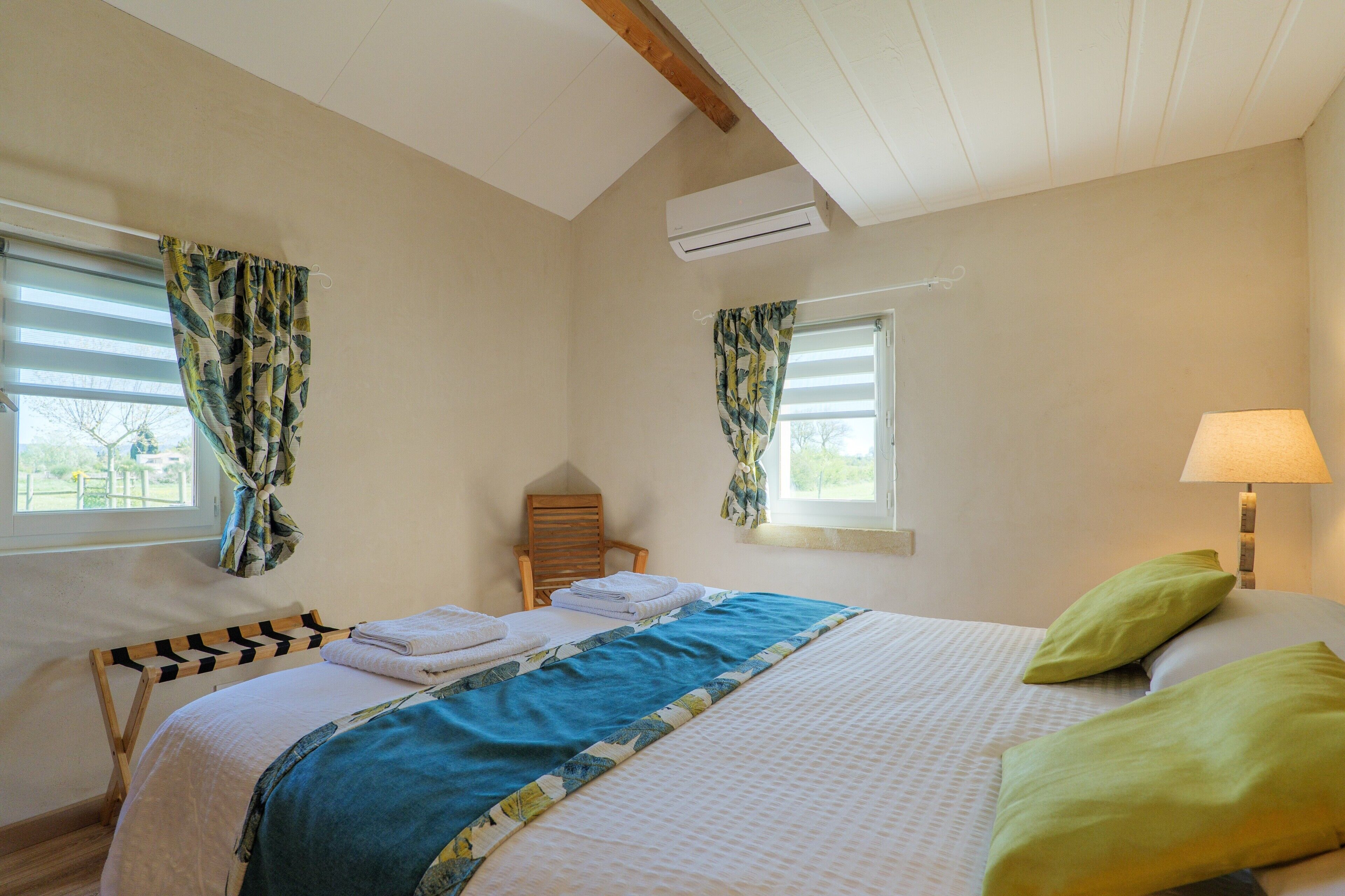A bedroom with a bed, a chair, a window, and a lamp.