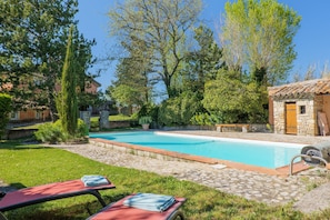 A swimming pool with a stone border, surrounded by a grassy lawn and trees.