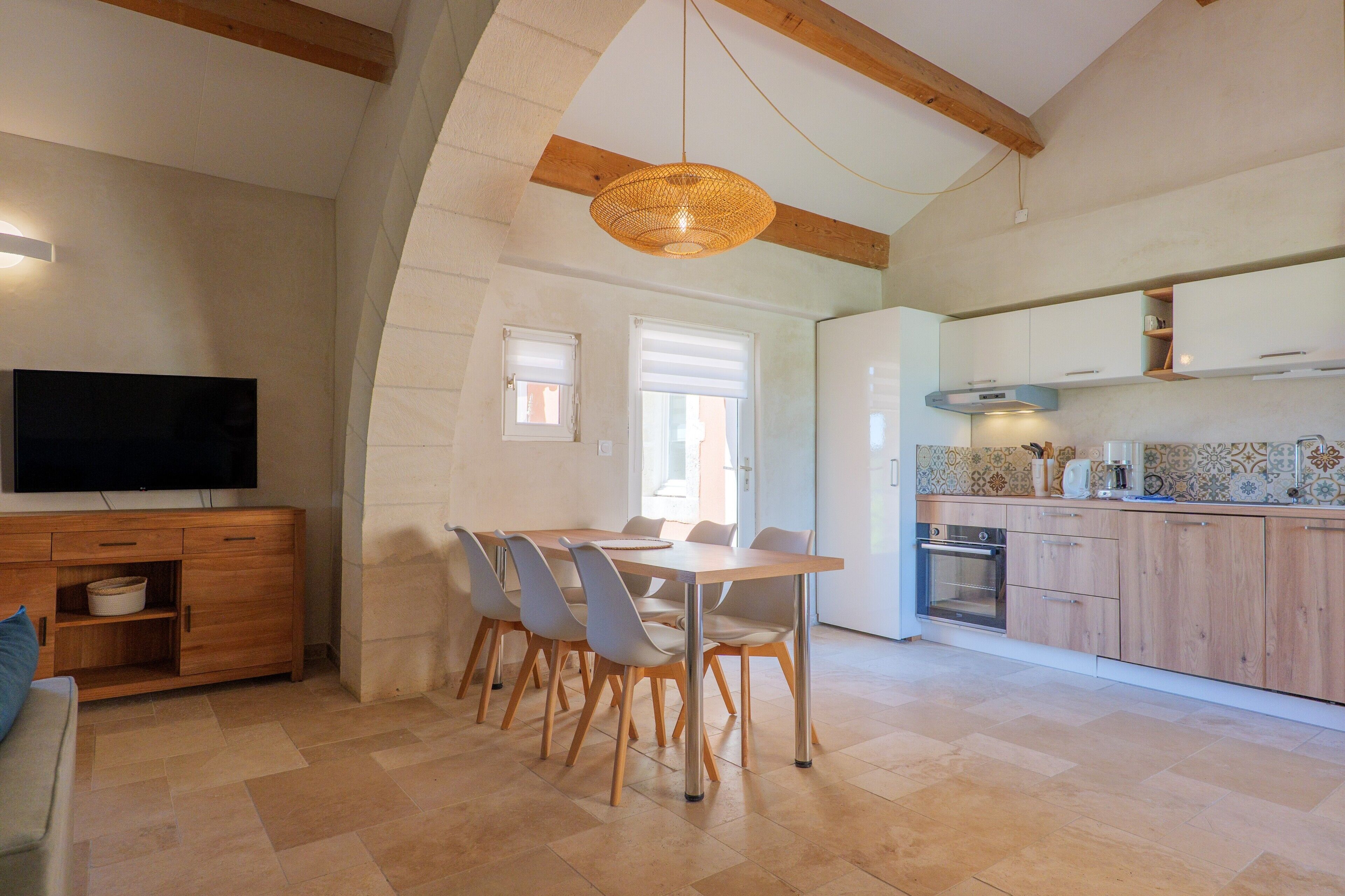 A modern kitchen with a dining area, wooden cabinets, and a television.