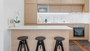 Eine moderne Küche mit Holzausstattung, einem Einbauofen, einer Spüle und drei schwarzen Barhocker.