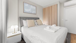 Ein modernes Hotelzimmer mit einem großen Bett, einem Nachttisch mit Lampe, einem gerahmten abstrakten Kunstwerk über dem Bett, einer Wand aus Holzpaneelen und einer weißen Tür.