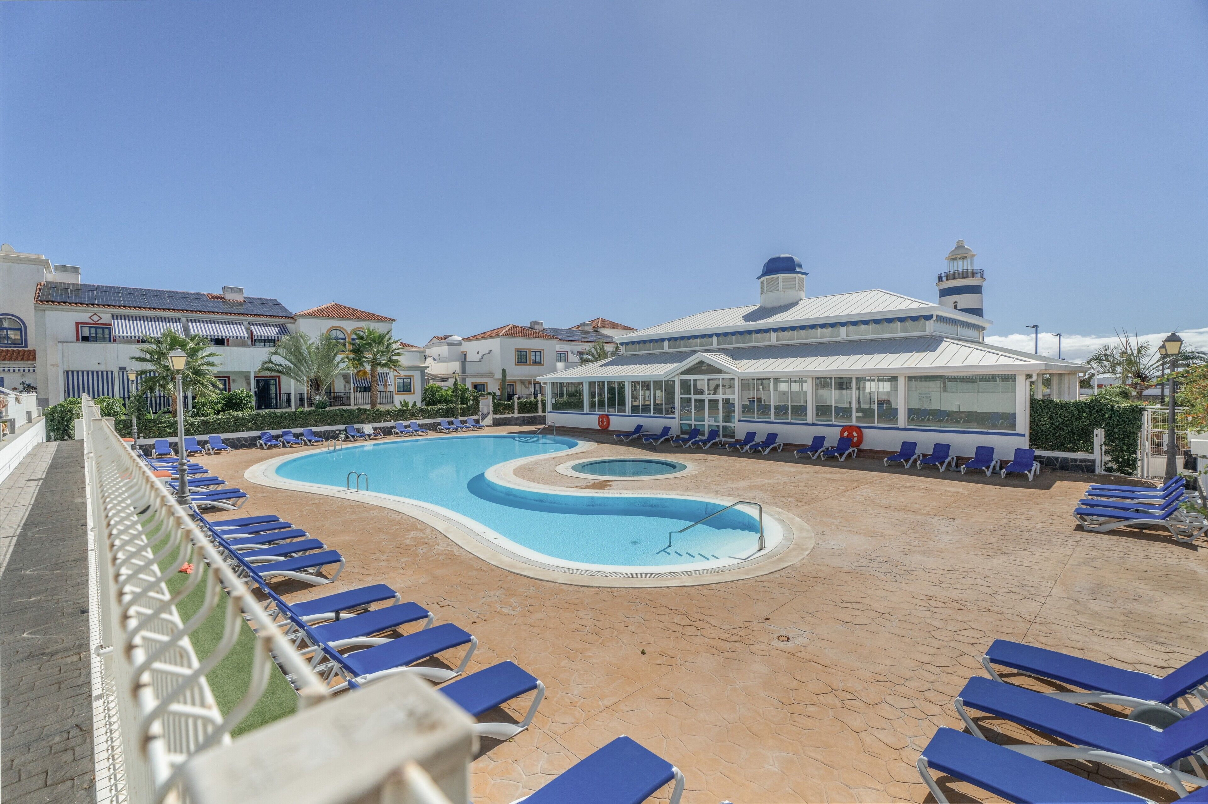 Une piscine avec des chaises longues bleues, un bâtiment surmonté d’un dôme et un phare en arrière-plan.