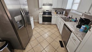 A modern kitchen with white cabinets, stainless steel appliances, and a tiled floor.