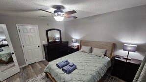 A bedroom with a bed, a ceiling fan, a dresser, a mirror, and two bedside lamps.