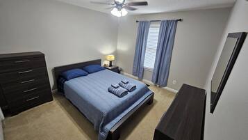 Une chambre à coucher comprenant un lit, une commode, une table de chevet, une lampe et un ventilateur de plafond.